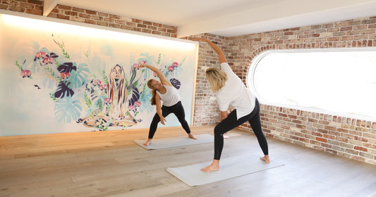 Yoga class practicing side stretch in a light-filled studio featuring hand-painted mural wallpaper by Hannah Chloe, designed for a calm and creative wellness space.