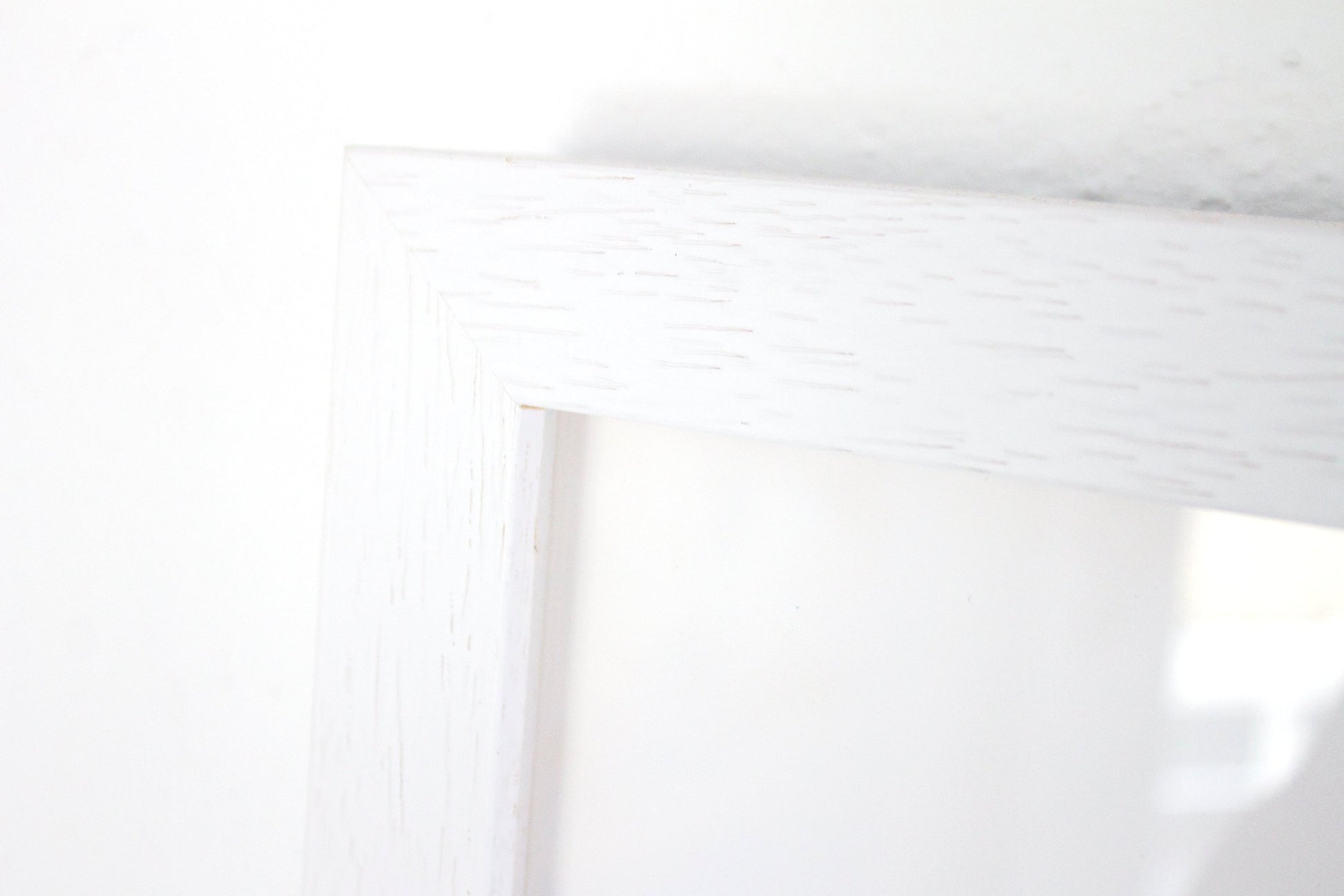 Close up detail of a white frame with woodgrain on a white background.