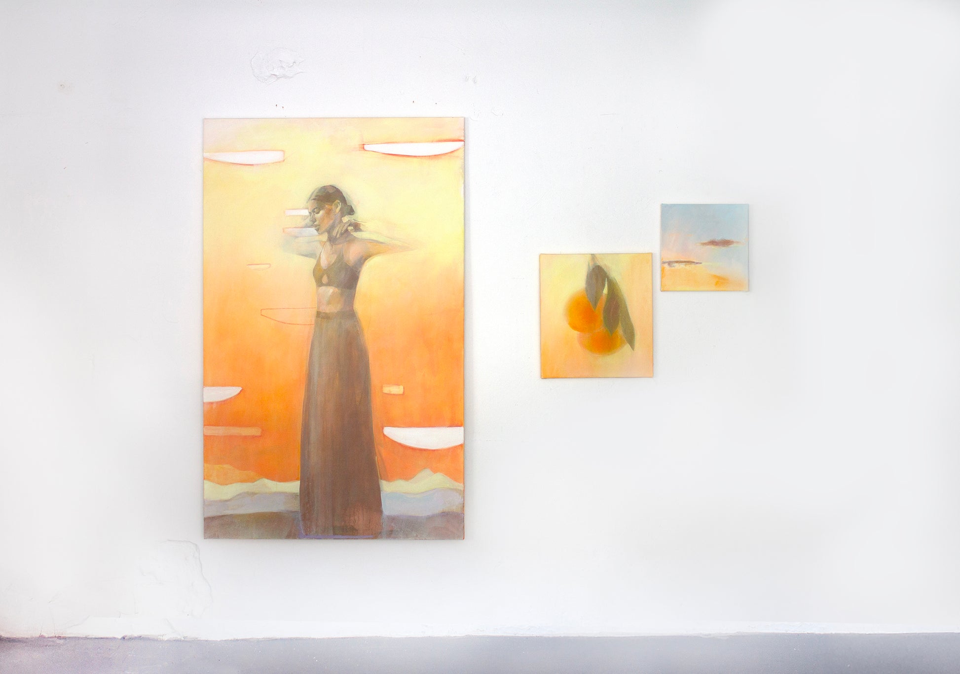 Gallery wall with warm abstract paintings including figure art, orange still life, and sunset landscape wall art in golden tones.