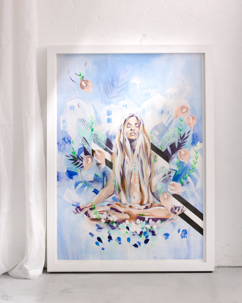 A print of Blue hues with a woman meditating in nature. In a white frame on a white wall with a curtain.