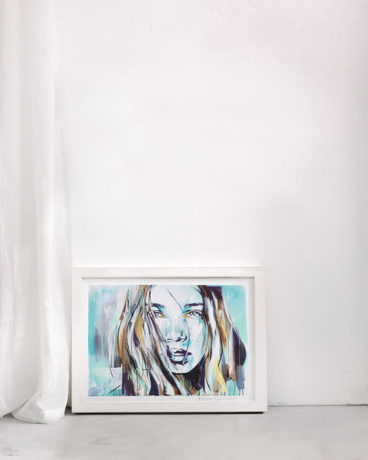 Bohemian portrait in turquoise of a woman showing a subtle strength. In a white frame in a plain room.