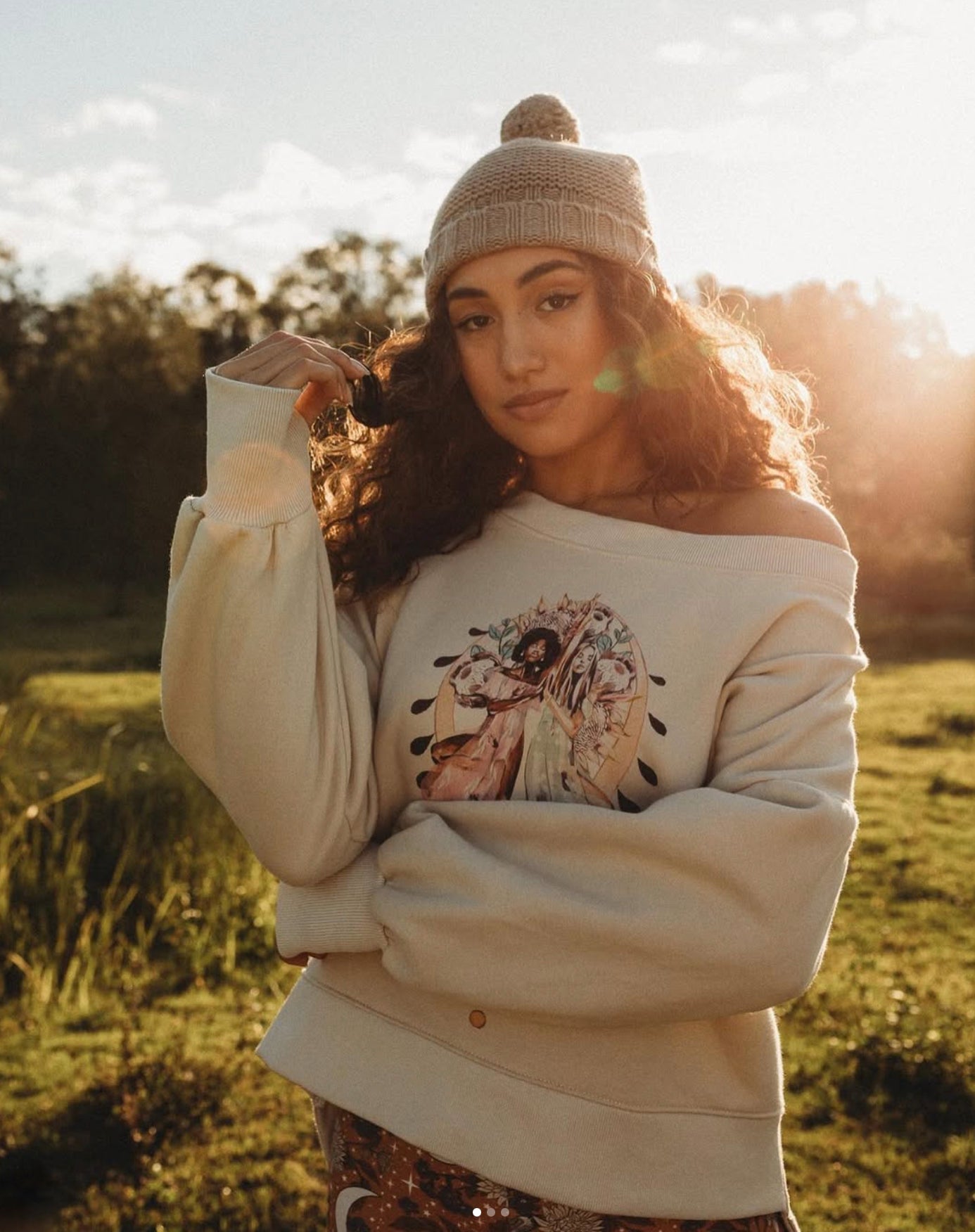 Woman wearing the Grounded organic cotton sweatshirt by Studio Hannah Chloe, featuring an art-inspired yoga print, photographed outdoors in warm sunlight.